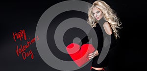 Beautiful woman with long blond hair standing on a black background dressed in red underwear and holds in his hands