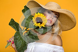 Beautiful woman with long blond hair, wearing a white dress and hat, holding sunflowers.