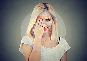 Beautiful woman with long blonde hair wearing white t-shirt, looking shy with hand on face and smiling