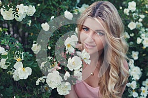 Beautiful woman with long curly hair smells white roses outdoors, closeup portrait of sensual girl face