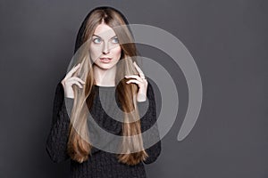 Beautiful woman with long, gorgeous dark blond hair. She is dressed in warm gray knit dress with a hood.