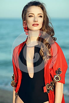 Beautiful woman standing at the seaside wearing trendy one piece halter neck swimsuit and red oriental beach cover up