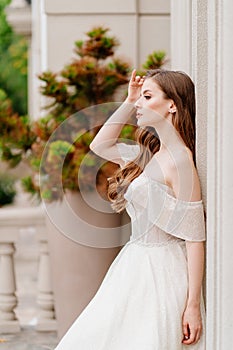 beautiful woman with long hair in wedding dress stands at wall of building.