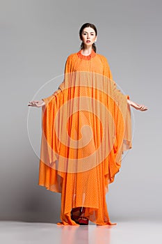 Beautiful woman in long orange dress posing dramatic in the studio