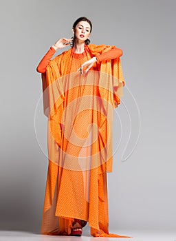 Beautiful woman in long orange dress posing dramatic in the studio