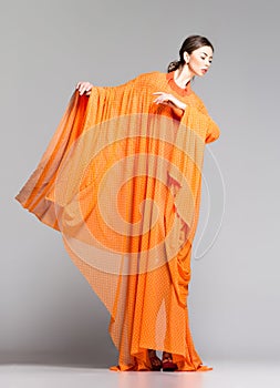 Beautiful woman in long orange dress posing dramatic in the studio