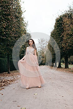 Beautiful woman in long rose evening dress walking path in park.