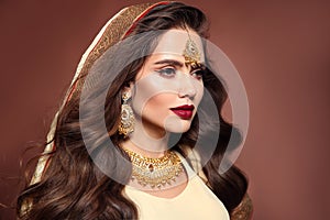 Beautiful woman with long wavy hair style and bright makeup. Young hindu brunette model with kundan golden jewelry set isolated on