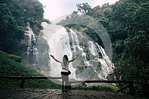 Beautiful woman looking at big waterfall after hiking in Chiang Mai & x28;Thailand& x29; arms spread