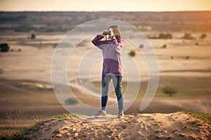 Beautiful woman looking through binoculars outdoors at sunset