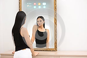 Beautiful woman looking at herself in smart mirror indoors