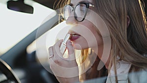 Beautiful woman looking in rear view mirror and applying red lipstick in car