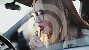 Beautiful woman looking in rear view mirror and applying red lipstick in car