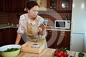 Beautiful woman looking through recipe for pickling fresh vegetables, comparing ingredients standing at kitchen island