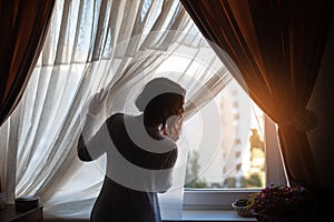 Beautiful woman looking through the window in dark room