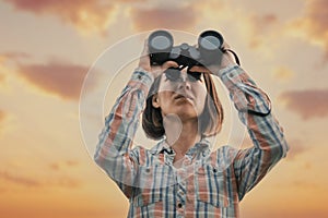 Beautiful woman looks through binoculars during sunset.