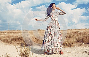 Beautiful woman in luxurious floral dress posing in summer field