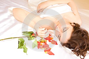 Beautiful woman lying in bed and looking at the petals