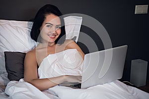 Beautiful woman lying in bed and making a phone call. Young girl using her laptop at home. Beautiful woman relaxing at