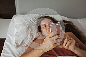 Girl with long hair lies bed looks into phone