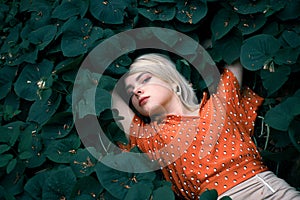 Beautiful woman lying among darkgreen plants, pretty girl relaxing outdoor. Close-up