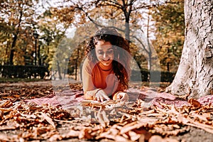 A beautiful woman lying down on a blanket on the ground while enjoying a book. She is smiling while reading. It`s a wonderful