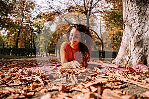 A beautiful woman lying down on a blanket on the ground while enjoying a book. She is smiling while reading. It`s a wonderful