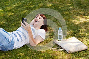 Beautiful woman lying in grass smiling with smart phone
