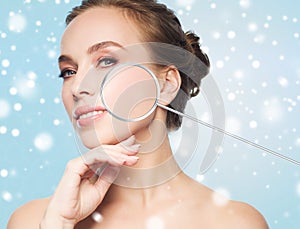 Beautiful woman with magnifier on face over snow
