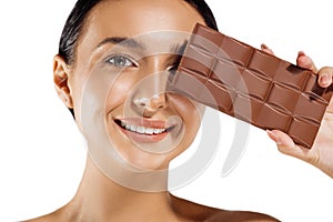 Beautiful woman with makeup holding a chocolate bar on her face, isolated on white background. Spa chocolate mask