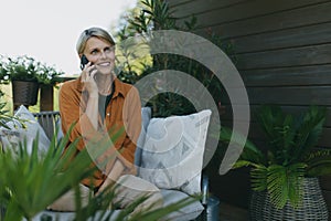 Beautiful woman making call outdoors, sitting on patio chair. Mother having moment to herself while her child is