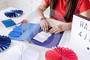 Beautiful woman making DIY paper fans of red and blue colors, celebrating Independence day of the USA. Happy 4 July the