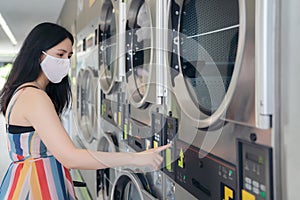 Beautiful woman with mask doing laundry at laundromat shop photo