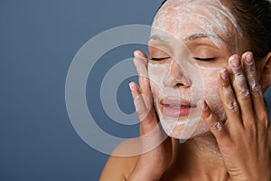 Beautiful woman massaging her face while removing make-up using a foam cleansing cosmetic product, and refreshing her skin with an