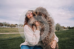 A beautiful woman is in the meadow with her dog. The owner is hugging her pet while the dog is licking her face.They are enjoying