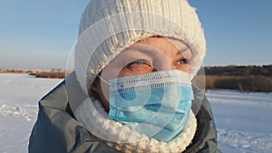 A beautiful woman in a medical mask walks in a winter park, wearing a medical mask in public places helps prevent the development