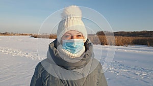 A beautiful woman in a medical mask walks in a winter park, wearing a medical mask in public places helps prevent the development