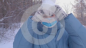 A beautiful woman in a medical mask walks in a winter park, wearing a medical mask in public places helps prevent the development