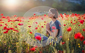 A beautiful woman meditates on a poppy field at sunset