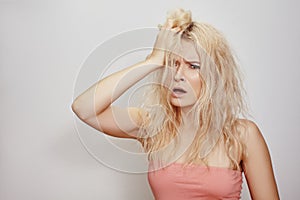 Beautiful woman with messed up hair. Unhappy grimacing face. Blond bleaching hairstyle with problem brittle hair