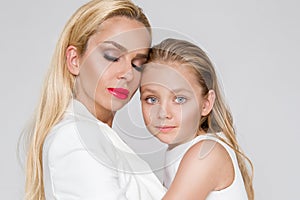 Beautiful woman mother with daughter snuggling together and show love, smartly dressed in a white dress