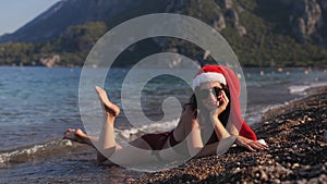 Beautiful woman Mrs. Claus in bikini and sunglasses lying on the beach