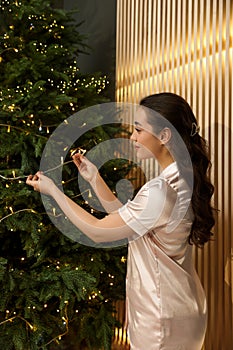 Beautiful woman near Christmas tree with golden lights indoors