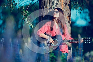 Beautiful woman near the tree and the field with lupine playing guitar