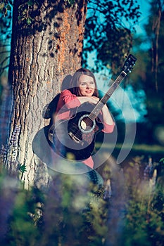 Beautiful woman near the tree and the field with lupine playing guitar