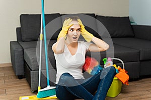A beautiful woman next to cleaning products and equipment is sitting on the floor and screaming, holding on to her head. A young
