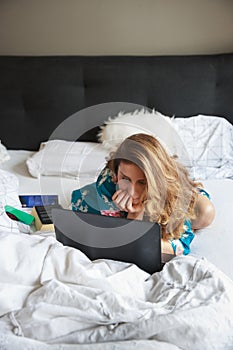 Beautiful woman in a night gown, lying in bed, working on computer