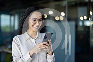 Beautiful woman in the office, happy and smiling latin american business woman uses internet phone close up, female