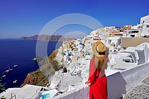 Beautiful woman in Oia village holds hat when looking cityscape from terrace in Santorini Island, Greece