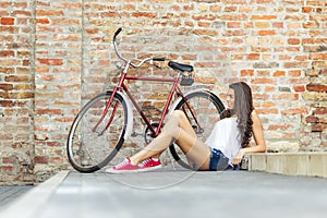 Beautiful woman with old bike in front of a brick wall